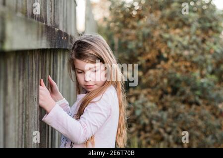 Junges Mädchen hält an einem Holzzaun im Hinterhof Stockfoto