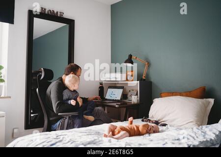 Papa mit Kind auf dem Schoß zu Hause Büro während covid Quarantäne Stockfoto