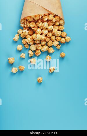 Karamell Popcorn in einem Papierumschlag auf blauem Hintergrund. Köstliches Lob für das Ansehen von Filmen, Serien, Cartoon. Freier Speicherplatz, Nahaufnahme. Minimalis Stockfoto