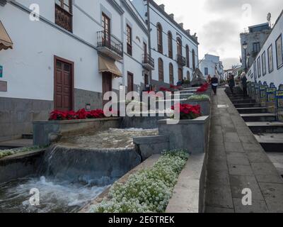 Firgas, Gran Canaria, Kanarische Inseln, Spanien 13. Dezember 2020: Blick auf die Straße Paseo de Gran Canaria mit Wasserfall Brunnen, Blumen und Keramik Stockfoto