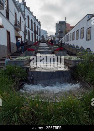 Firgas, Gran Canaria, Kanarische Inseln, Spanien 13. Dezember 2020: Blick auf die Straße Paseo de Gran Canaria mit Wasserfall Brunnen, Blumen und Keramik Stockfoto