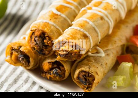 Hausgemachte mexikanische Chicken Flautas mit Crema und Salat und Tomaten Stockfoto