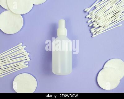 Weiße Plastikflasche ohne Marke mit Desinfektionsmittel, Wattestäbchen und Sticks auf violettem Hintergrund. Natürliche Bio-Spa-Kosmetik und flüssige antimikrobielle Co Stockfoto