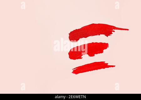 Drei Abstriche von mattem roten Lippenstift auf rosa Hintergrund, Kosmetik-Konzept. Draufsicht, Lifestyle. Stockfoto