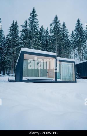 Moderne Holzhütte und schneebedeckte Bäume im Winter Finnland Lappland. Abgeschiedenes kleines Haus. Privates Haus in der Nähe von Wald. Landhaus. Stockfoto