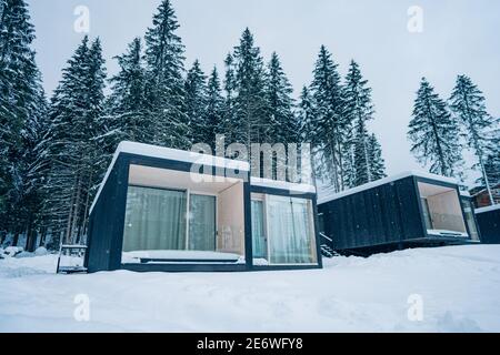 Moderne Holzhütte und schneebedeckte Bäume im Winter Finnland Lappland. Abgeschiedenes kleines Haus. Privates Haus in der Nähe von Wald. Landhaus. Stockfoto