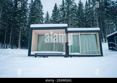 Moderne Holzhütte und schneebedeckte Bäume im Winter Finnland Lappland. Abgeschiedenes kleines Haus. Privates Haus in der Nähe von Wald. Landhaus. Stockfoto