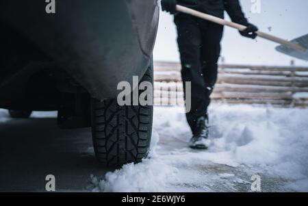 Sammeln von Schnee mit einer Schaufel auf einer öffentlichen Straße, um sein Auto nach starkem Schneefall zu benutzen. Widrige Wetterbedingungen Stockfoto