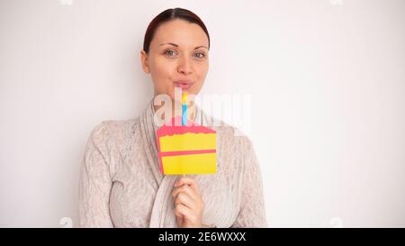 Porträt einer Frau, die eine Kerze auf einem gefälschten Pappkuchen ausbläst. Negativer Leerzeichen oder Kopierraum für Text. Stockfoto