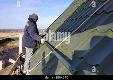 Der Meister arbeitet auf einem Dach ohne Versicherungselemente, einem grünen Dach, einer Metallfliese. Privates Haus auf dem Land. Stockfoto