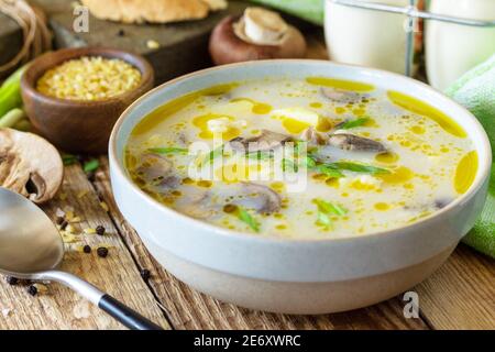 Pilzsahnesuppe mit Bulgur und Sahne auf rustikalem Tisch aus nächster Nähe. Stockfoto
