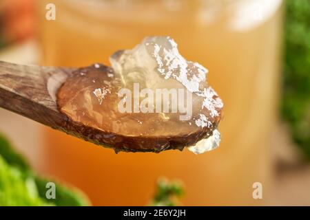 Gekühlte Rinderbrühe mit Gelierung auf einem Löffel, mit einem Glas voller Brühe im Hintergrund Stockfoto