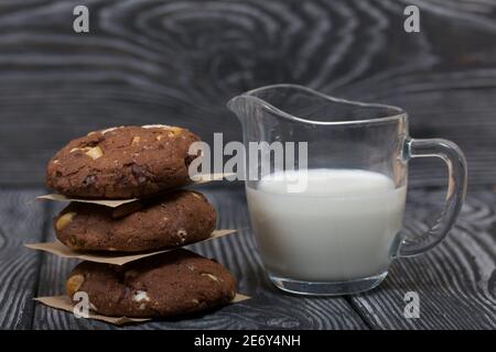 Haferflocken Kekse mit Erdnüssen und Schokolade. In einer Säule gefaltet und mit Papier ausgelegt. Milch in der Nähe. Auf Kiefernbrettern. Stockfoto