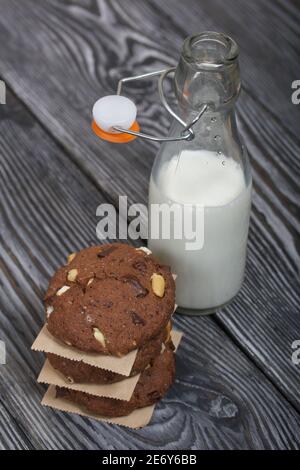 Haferflocken Kekse mit Erdnüssen und Schokolade. In einer Säule gefaltet und mit Papier ausgelegt. Milch in der Nähe. Auf Kiefernbrettern. Stockfoto