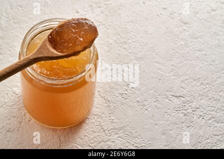 Abgekühlte Rinderknochenbrühe in einem Glasgefäß und auf einem Löffel, auf weißem Hintergrund mit Kopierraum Stockfoto