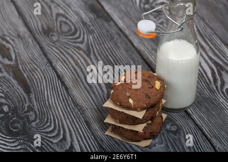 Haferflocken Kekse mit Erdnüssen und Schokolade. In einer Säule gefaltet und mit Papier ausgelegt. Milch in der Nähe. Auf Kiefernbrettern. Stockfoto