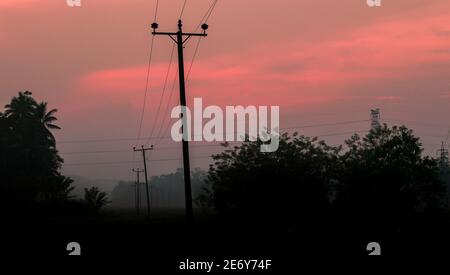 Ländliche Dorf am frühen Morgen Nebel und malerischen roten Himmel Wolken Landschaft Foto. Nicht so gerade hölzerne elektrische Pole in das Reisfeld, fährt Stockfoto