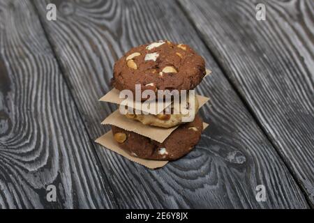 Haferflocken Kekse mit Erdnüssen und Schokolade. In einer Säule gefaltet und mit Papier ausgelegt. Auf Kiefernbrettern. Stockfoto