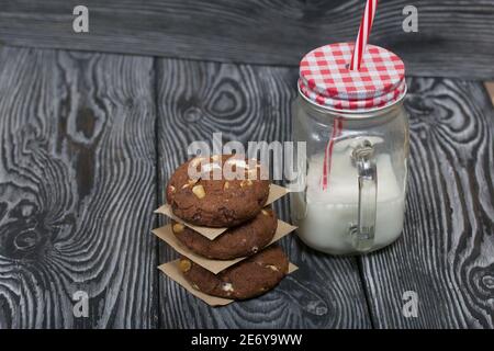Haferflocken Kekse mit Erdnüssen und Schokolade. In einer Säule gefaltet und mit Papier ausgelegt. Milch in der Nähe. Auf Kiefernbrettern. Stockfoto