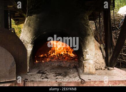 Innenansicht eines Holzofens Pizza Ofen mit freiliegendem Feuer Ziegel und gewölbte Decke. Flamme im Ofen. Stockfoto