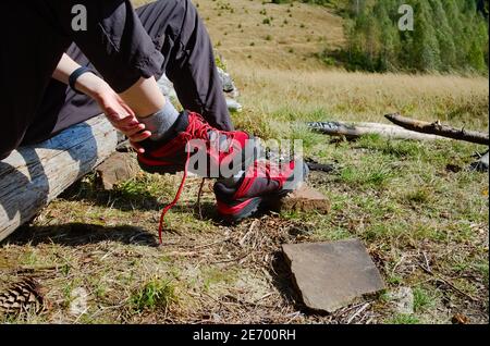 Junge Reisende Mädchen, die Wanderschuhe auf Camping während des Wanderns in den Bergen. Wanderschuhe aus Trekkingstiefeln, während sie auf Holzbalken sitzen. Stockfoto