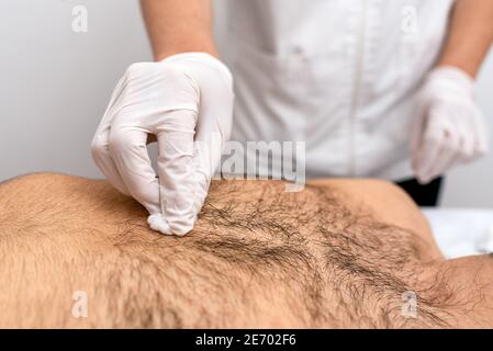 Nahaufnahme eines unerkannten Arbeiters, der ein Verfahren mit Baumwolle und Alkohol bei einem männlichen Klienten macht. Stockfoto