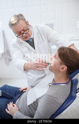 Vertikale Aufnahme eines älteren Zahnarztes, der in seiner Klinik arbeitet und die Zähne des Patienten überprüft Stockfoto