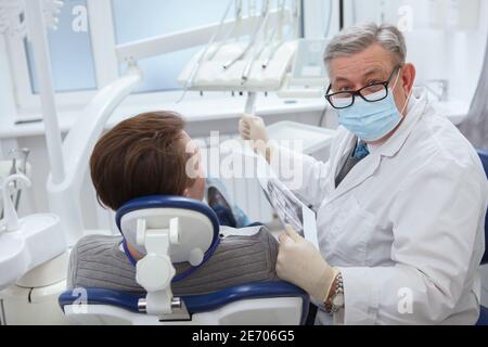 Senior männlichen Zahnarzt trägt medizinische Gesichtsmaske, Blick auf die Kamera während der zahnärztlichen Termin mit dem Patienten Stockfoto