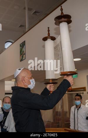 Jerusalem, Israel - 28. Januar 2020: Ein Mann, der eine Schutzmaske trägt und eine tora-Schriftrolle in einer Jerusalemer Synagoge aufhebt. Stockfoto