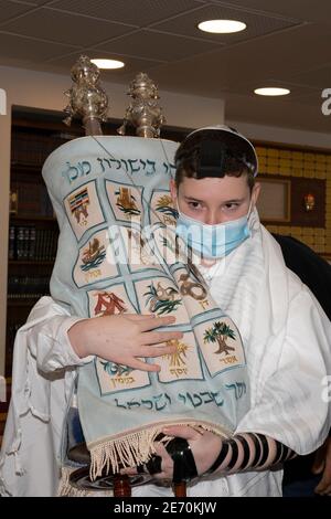 Jerusalem, Israel - 28. Januar 2020: Ein Barmizwa-Junge mit einer tora-Schriftrolle mit Tefillin und einer Schutzmaske in einer Jerusalemer Synagoge. Stockfoto