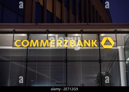 Commerzbank-Logo auf einem gelb beleuchteten Gebäude. Bankfiliale in Deutschland. Fassade eines modernen Büros mit großen Glasfenstern. Stockfoto