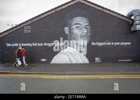 Fußgänger passieren das Wandbild des Manchester United Fußballspielers Marcus Rashford an der Seite eines Gebäudes in Withington, Manchester. Stockfoto