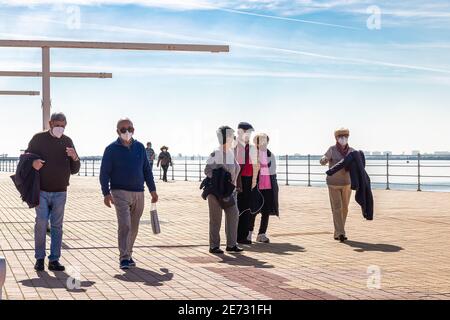 Huelva, Spanien - 27. Januar 2021: Ältere Menschen, die an der Huelva Promenade spazieren, während des Alarmzustandes und des Quarans schützende oder medizinische Gesichtsmasken tragen Stockfoto