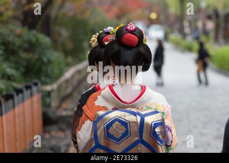 Zwei Frauen, die als Geisha gekleidet sind, gehen im Herbst die Shinbashi-dori-Straße hinunter. Stockfoto