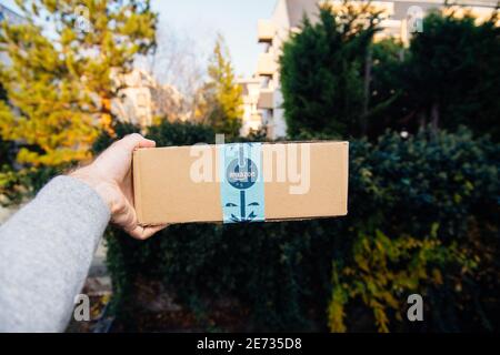 Paris, Frankreich - Nov 16, 2018: POV persönliche Perspektive männliche Hand mit Amazon Prime Karton mit festlichem Feiertag Scotch Tape - unfokussierte Stadt Hintergrund Stockfoto