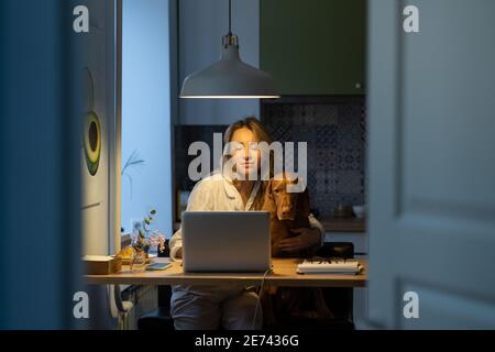 Frau im Schlafanzug sitzt mit Hund auf Stuhl zu Hause Remote-Arbeit am Laptop während der Selbstisolierung Stockfoto