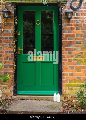 Milch wird vor der Haustür eines Hauses in Berkshire mit einer grünen Tür gelassen. Stockfoto