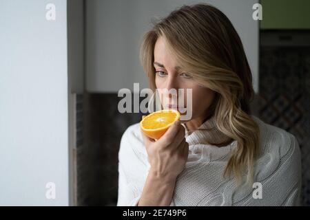 Kranke Frau, die versucht, den Geruch der halben frischen Orange zu spüren, hat das Symptom von Covid-19, den Verlust des Geruchs, den Geschmack Stockfoto