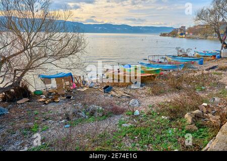 Bunte Boote stehen an der Küste von uluabat See mit Altstadt und riesigen Berg Hintergrund. 22,01.2021. Golyazi (Apolyont), Bursa, Türkei. Stockfoto