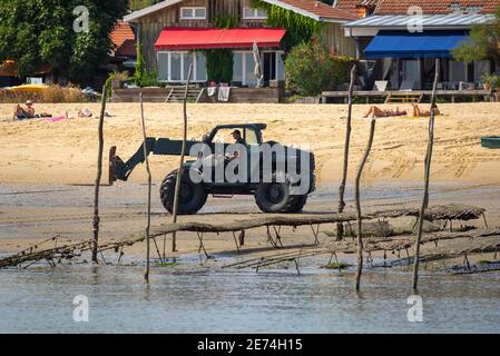 Ein Traktor arbeitet am Strand bei Ebbe in der Nähe von Cap Ferret. Austernfalle am Strand traditionelle Holzhäuser im Hintergrund Stockfoto