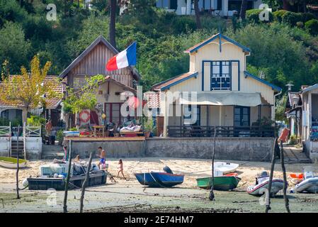 Typische Ferienhäuser in der Nähe von Cap Ferret im Bassin d'Arcachon, Frankreich. Im Sommer wurden Boote an der Küste aufgrund von Ebbe und einer französischen Flagge befahren Stockfoto