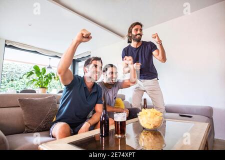 Eine Gruppe von Freunden, die ein Spiel im fernsehen ansehen, um die zu feiern Sieg ihres Teams Stockfoto