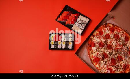 Nahaufnahme von appetitischem Sushi in Behältern und großer Pizza in Box auf orangefarbenem Hintergrund. Pizza und leckere Sushi-Brötchen mit verschiedenen Zutaten Stockfoto