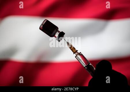 In dieser Abbildung ist ein Fläschchen mit Pfizer-BioNtech COVID-19 Impfstoff und eine medizinische Spritze über der österreichischen Flagge zu sehen. Stockfoto