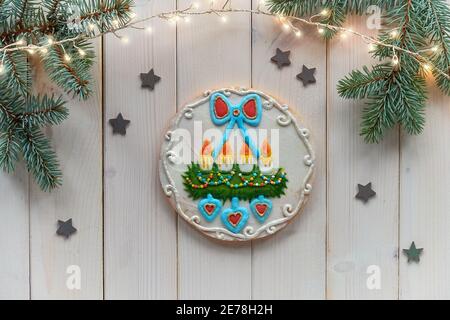 Dekorierter Lebkuchen mit Kerzen auf Advent Dekokranz mit Tannenzweigen. Weihnachten flach legen mit natürlichen Tanne, Sterne und Girlande von festlichen Lichtern Stockfoto