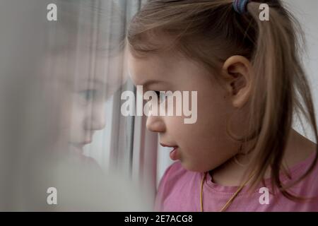 Kindheit, Einsamkeit, Isolation, Traurigkeit, Hoffnung Konzepte - eine traurige niedlich besorgt Kleinkind Baby Mädchen in rosa mit Pferdeschwänze Frisur schaut durch Stockfoto