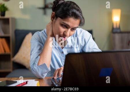 Junge Geschäftsfrau, die unter Nackenschmerzen leidet, während sie mit der Arbeit am Laptop beschäftigt ist - Konzept der Überarbeit, Belastung, gestresst, unbequeme Position oder Pos. Stockfoto