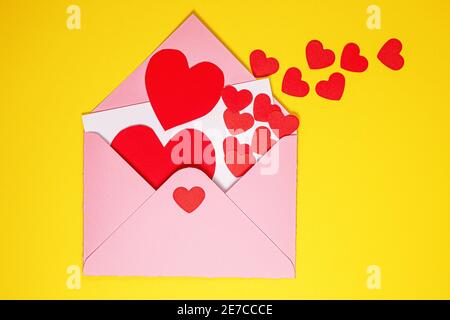 Valentinskarte. Papier rote Herzen fliegen aus rosa Papierumschlag auf gelbem Hintergrund. Papierkunst am valentinstag. Papier geschnitten und Handwerk Stil. Sp Stockfoto