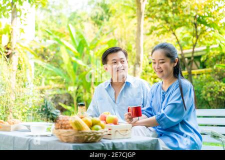 Seniorenpaar mit Essen und Trinken Picknick im Garten Park unterhalten Pflege zusammen, asiatische Rentnerpaar Stockfoto