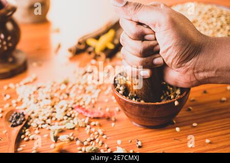 Nahaufnahme der Hände schlagen oder zerschlagen indischen gemischt Masala Gewürze in der Holzschale oder Gewürzmühle - Konzept Vorbereitung der indischen Masala Gewürze Stockfoto